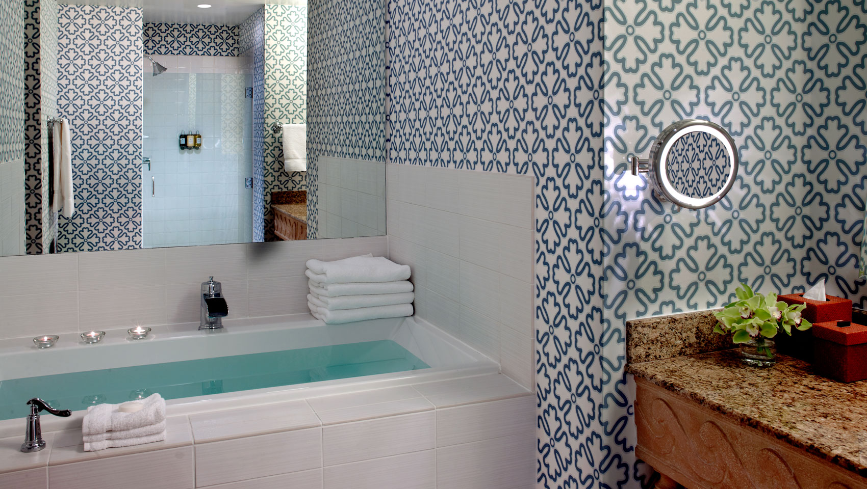 A spacious bathroom with a filled soaking tub adorned with candles and stacked towels.