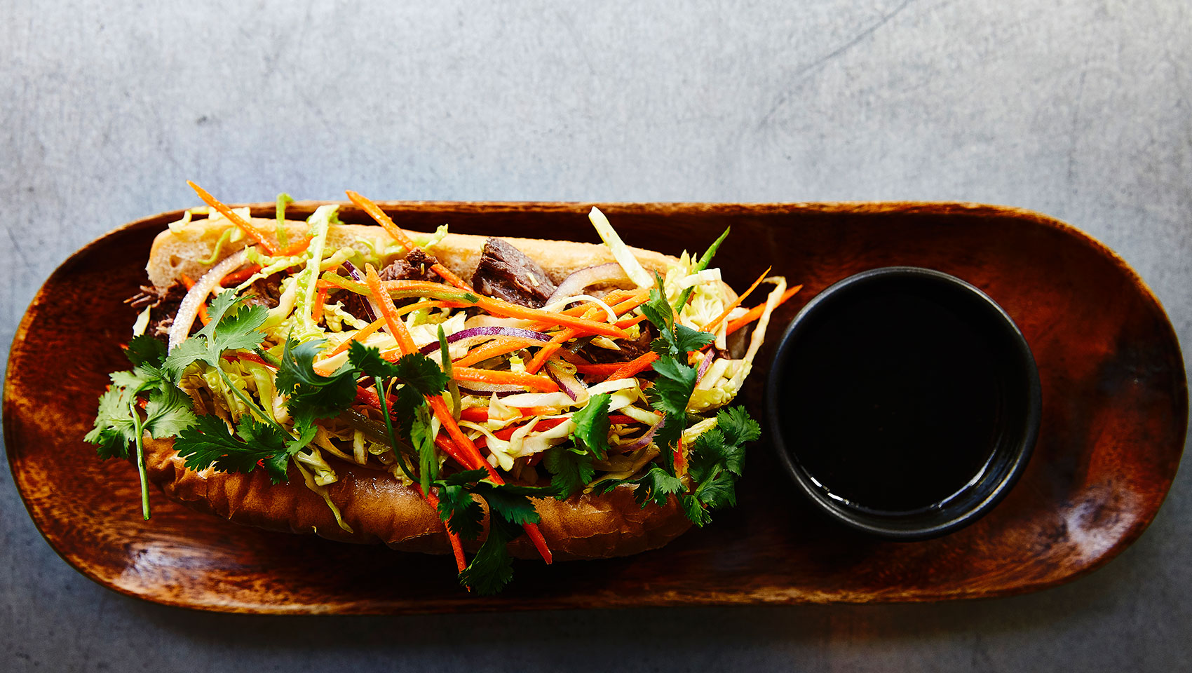 overhead view of sandwich and sauce dish on wooden plate